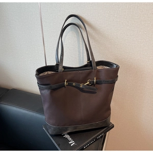 Detail of a large brown tote bag with leather straps and vintage gold metal buckles