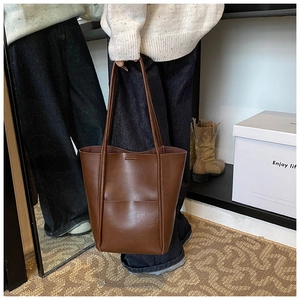 Close-up of the smooth dark brown leather texture and stitching on the bucket tote bag