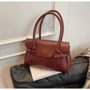 Detailed close-up of dark red leather shoulder bag with gold metal logo and side buckles