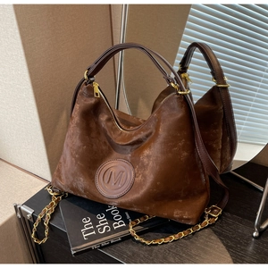 Détail du sac hobo en daim marron avec emblème M et bandoulières en cuir et chaîne