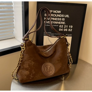 Détail du cabas vintage en daim marron avec logo M embossé et chaîne dorée