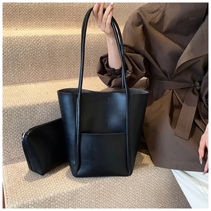 Detail of minimalist black leather bucket bag with matching zipper pouch on model