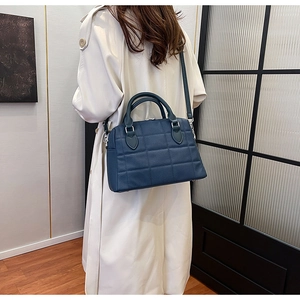 Close-up of a dark blue quilted shell handbag with a silver chain and stylish leather strap
