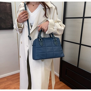Detail of navy blue quilted tote bag worn with a white trench coat in a modern setting