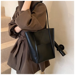 Detail of a minimalist black leather tote bag worn by a model in a brown trench coat