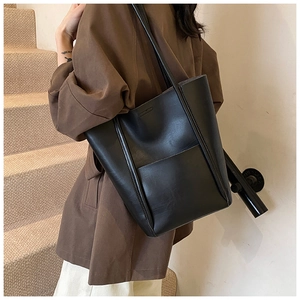 Detailed side view of a large black leather tote bag worn by a model in city style