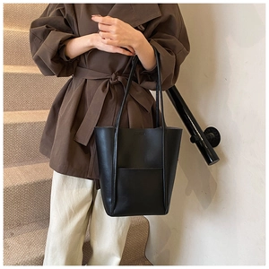 Detail of the black leather tote bag worn by a model in a sophisticated setting