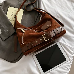 Detailed view of brown suede hobo bag with gold hardware and strap buckles on a desk