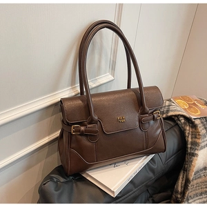 Detail of vintage brown PU leather shoulder bag with gold logo and metal buckle accents