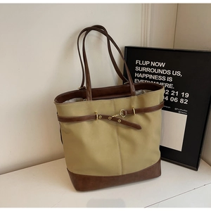 Detail view of large khaki tote bag with brown leather trim and gold buckle accent
