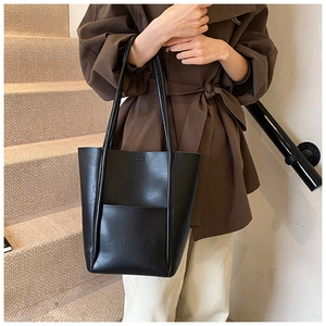 Chic black leather bucket tote bag with exterior pocket shown on model near stairs