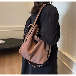 Detail view of a large brown suede bucket bag worn by a model in a minimalist setting