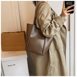 Close-up of the large brown leather tote bag showing matte texture and functional outer pocket