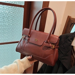 Detail of burgundy leather shoulder bag showing the golden buckles and textured flap