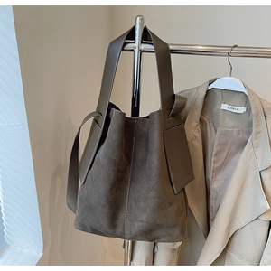 Detailed view of the dark brown suede bucket bag with wide strap and side leather accents