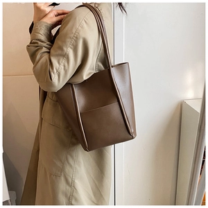 Brown leather bucket tote bag shown on a model wearing a classic trench coat