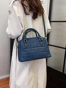 Navy blue quilted tote bag with cross-body strap worn on a beige trench coat