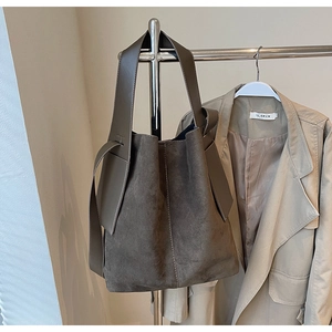 Detail of premium brown suede tote bag with leather strap on a minimalist clothing rack