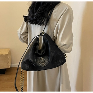 Détail du sac cabas noir avec logo M gaufré et bandoulière en chaîne dorée tressée