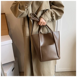 Brown leather tote bag worn as a shoulder bag showing large capacity and matte finish