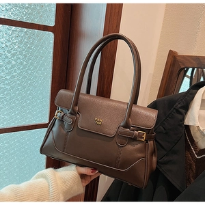 Detail of dark brown leather tote with gold metal logo and decorative buckle