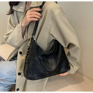 Détail du sac hobo noir avec logo M gaufré et chaîne en métal doré élégante sur la bandoulière