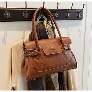 Brown leather tote bag featuring a gold logo on a beige trench coat and scarf background