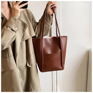 Detail view of a large brown faux leather tote bag worn with a stylish khaki trench coat