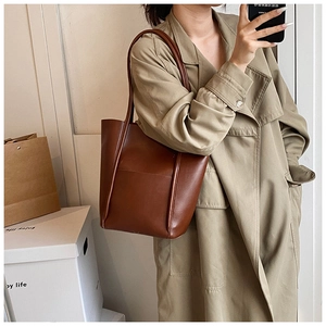 Detailed close-up of brown leather tote bag with vertical stitching on khaki coat