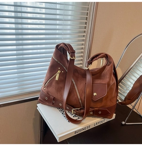 Detail of caramel brown suede tote bag with metal zippers and buckles on books