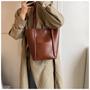 Detail of dark brown leather tote bag with exterior pocket worn with khaki trench coat