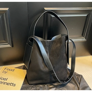 Detail of black leather bucket bag with textured panels on dark wooden background