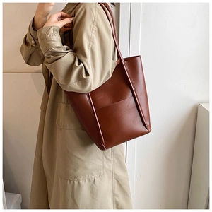 Detailed side view of a brown leather bucket tote bag worn with a khaki trench coat