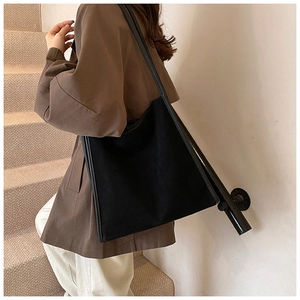 Detail einer großen schwarzen Wildleder-Shopper-Tasche mit Lederbesatz an einem Modell