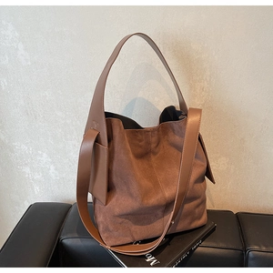 Detail of a brown suede hobo tote bag with leather straps on a black leather bench