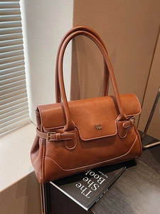 Retro brown leather underarm bag with gold logo on a desk with natural window light