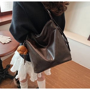 Détail du sac seau vintage marron foncé avec texture cuir et charm ours en peluche sur l'épaule