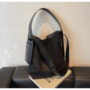 Detail of black suede and matte leather tote bag with square charm on a dark bench