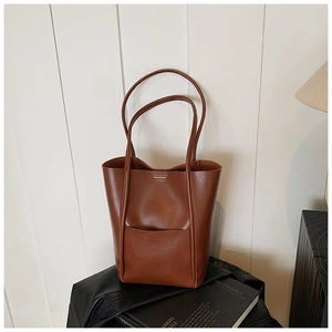 Detail of dark brown leather tote bag showing a front pocket and slender shoulder straps
