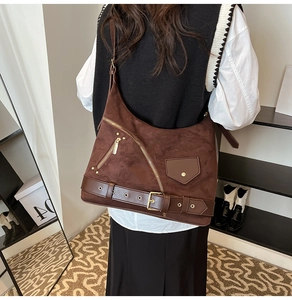 Detail of dark brown suede shoulder bag with industrial zipper pockets and buckle straps