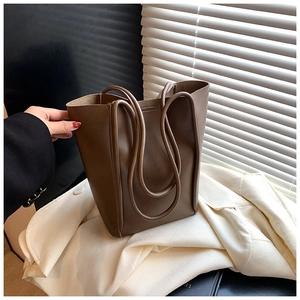 Close-up of a brown leather bucket tote bag on a blazer in soft natural lighting