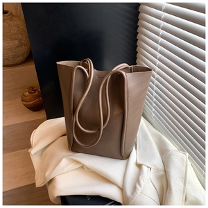 Close-up of minimalist brown bucket tote bag on white blazer with soft lighting