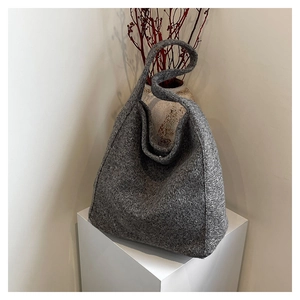 Artistic display of a grey wool texture shoulder bag on a minimalist pedestal with decor