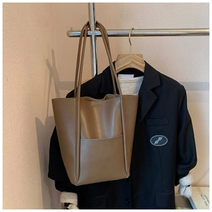 Brown faux leather tote bag with long straps and front pocket shown in a lifestyle setting