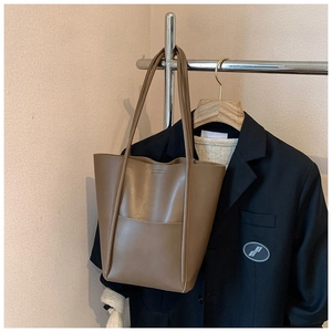 Detail view of large brown bucket tote bag hanging next to elegant business attire
