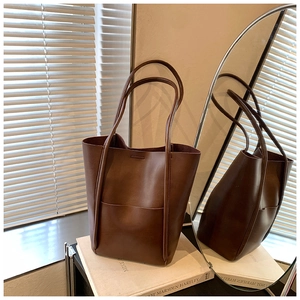 Close-up of a large dark brown leather tote bag with pocket in a minimalist setting