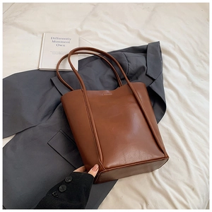Detailed view of brown leather tote bag with vertical stitching on a grey blazer