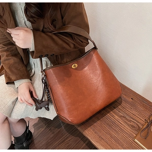 Detail of a brown leather tote bag featuring a gold metal buckle and a pony charm