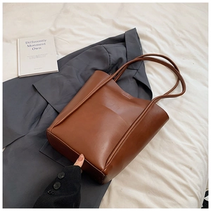 Detail of a large dark brown leather tote bag on a blazer, showing wide base and dual straps