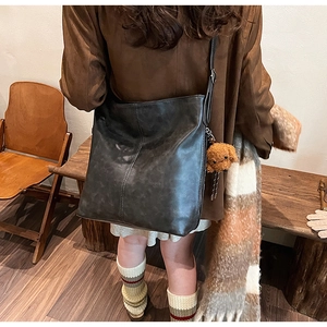 Détail d'un sac seau vintage en cuir noir avec un petit ours en peluche marron